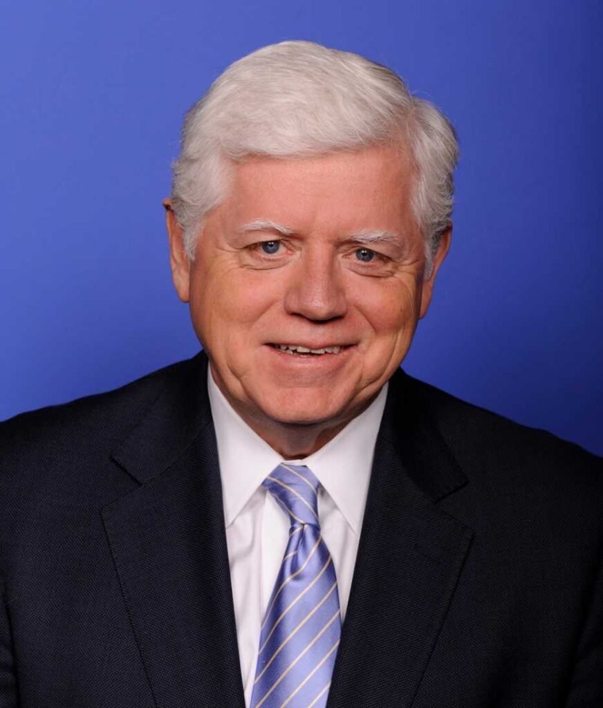 Man with white hair in suit and tie against blue background